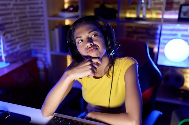 Jovem pensativa usando fone de ouvido em frente ao computador onde está jogando online